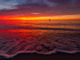 A sailboat sits on the horizon during a vibrant beach sunset in Venice, Florida.