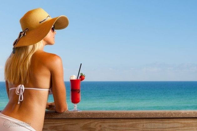 Hospitality photography of a woman in a floppy hat with a drink at a beach resort overlooking the water.