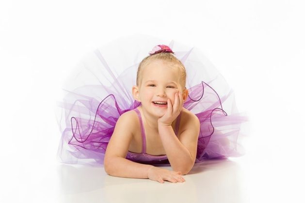 Portrait photography of a young ballerina in a tutu lying down and laughing.