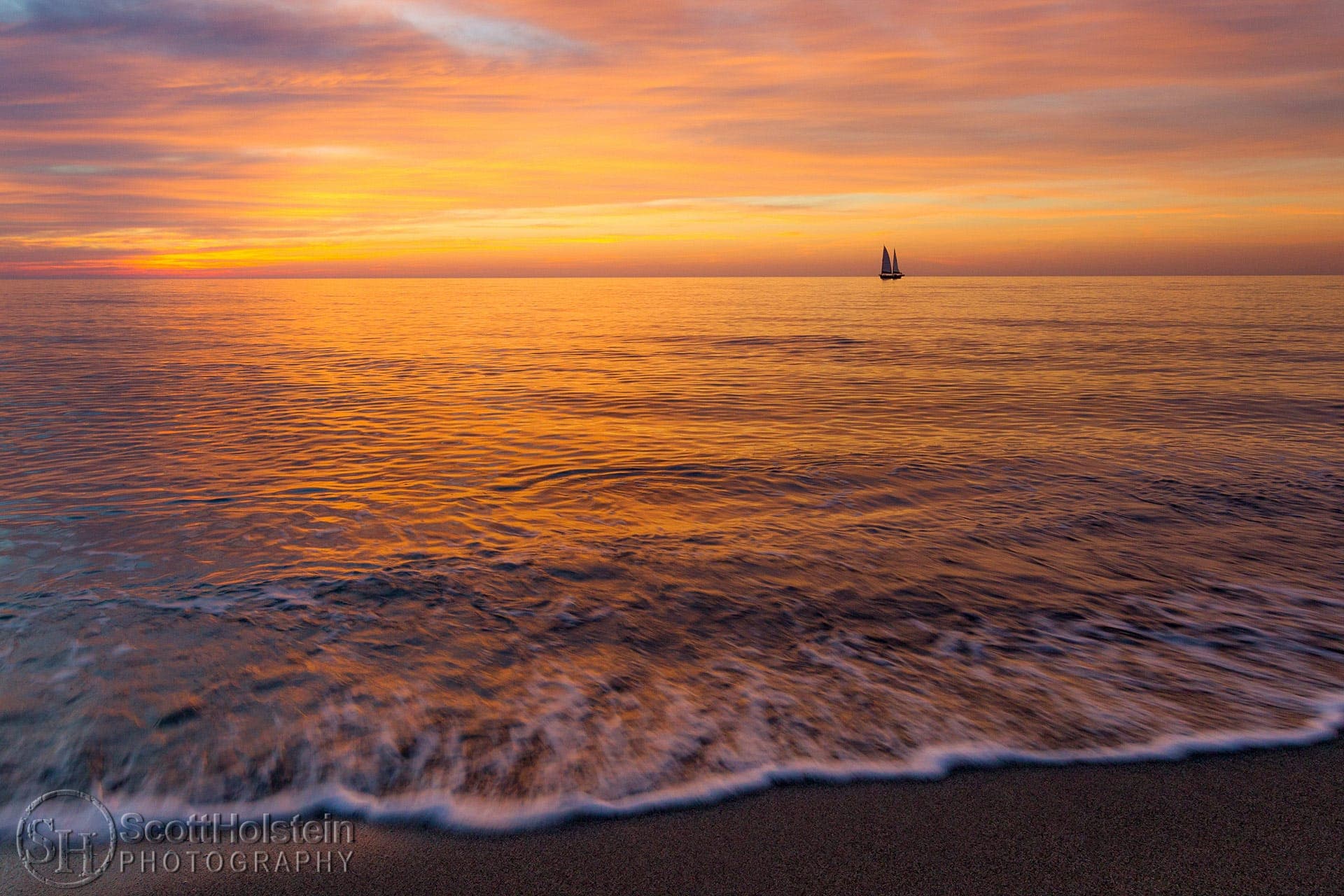 A sailboat punctuates a pastel-colored sunset in the Gulf of Mexico off of a Florida beach.