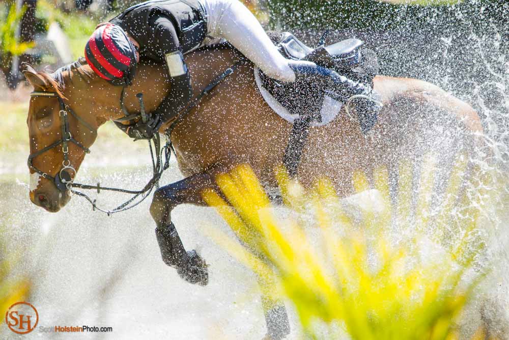 A rider is thrown from the saddle and clings to the horse's neck after the horse stumbled on a water jump.