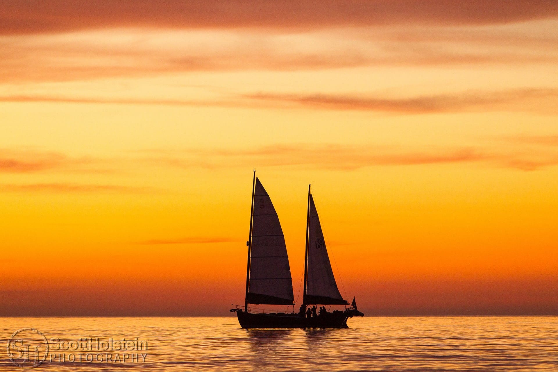 A sailboat is silhouetted in front of the afterglow of a yellow and orange sunset in the Gulf of Mexico in Venice, Florida.