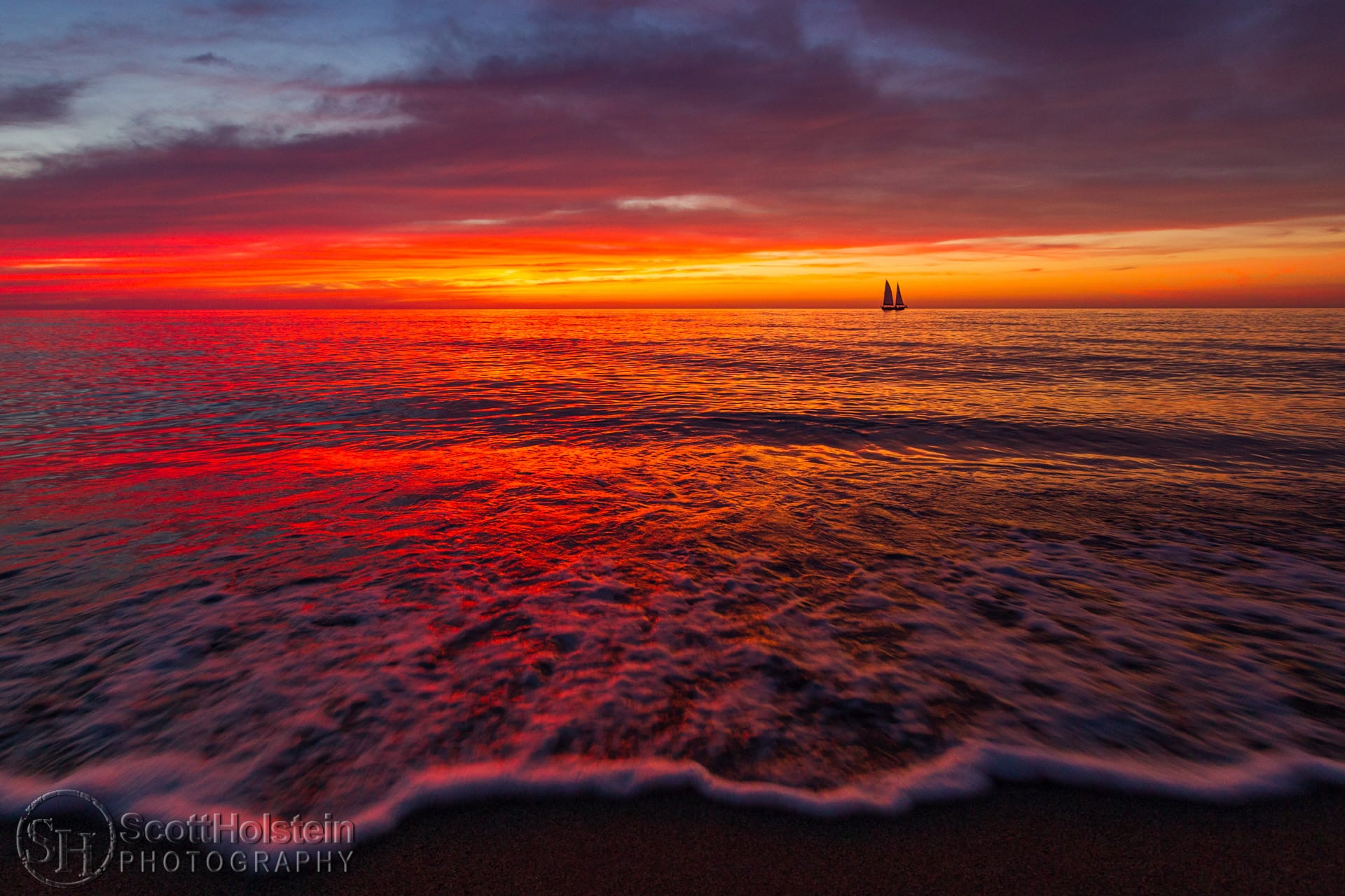 A sailboat sails during a vibrant sunset just off the beach in Venice, Florida.